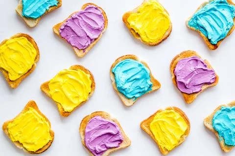 Funny toasted bread with colored cheese spread. Overhead view Stock Photos