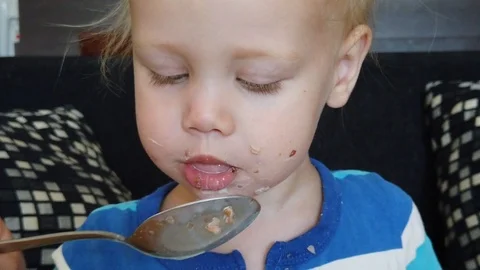 Funny two-year-old white child eats porridge with a large spoon. Vidéo 108132251