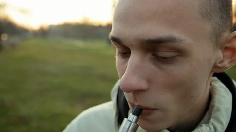 Funny wide angle closeup portrait of smoking e-cigarette young man in the park 動画素材 121061737