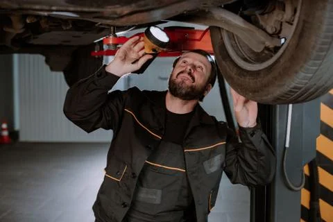 A funny worker analyzes the car from below, being very focused Stock Photos