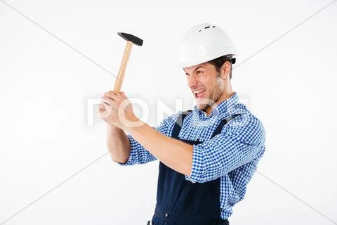 Funny young builder applying hummer to his head in helmet Stock Photos