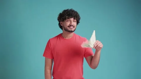 Funny young latin man with a pack of dollar in his hands on a blue studio Stock Footage 239776622