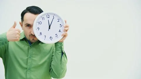 Funny young man hiding a half of face behind the clock, giving thumb up, making Stock Footage 130266138