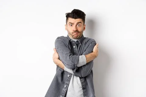 Funny young man hugging himself and grimacing, feeling embarrassed and exposed Stock Photos