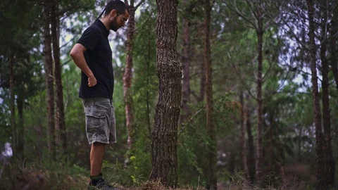 Funny Young Man magically disappears stepping behind a tree in the forest Stock Footage 89984398