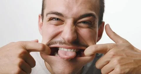 Funny young man with mustache pulling a silly face and sticking out his ton.. Stock Photos