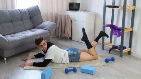 Funny young nerd man in glasses doing fitness exercise lying on floor at home. Stock Footage 153355983