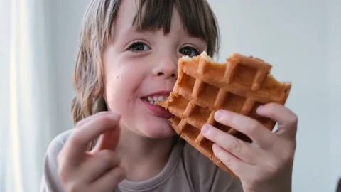 Funny young preschooler boy eats delicious waffle and smiles Video stock 156682583