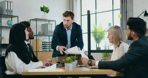 Furious 40-aged bearded ceo shouting on his quiet mixed race subordinates about Stock Footage 159593570
