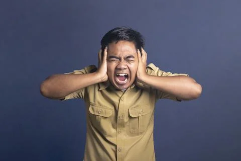 Furious or stressed young man in a khaki uniform shirt covering his ears wi.. Stock Photos