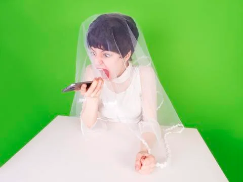 Furious young bride looking at her cell phone and screaming isolated on green Stock Photos
