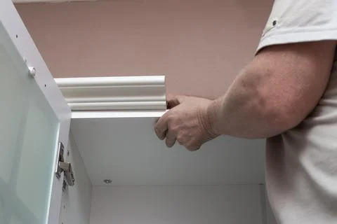 Furniture assembly. A man assembles a kitchen set, attaches stucco molding to Stock Photos
