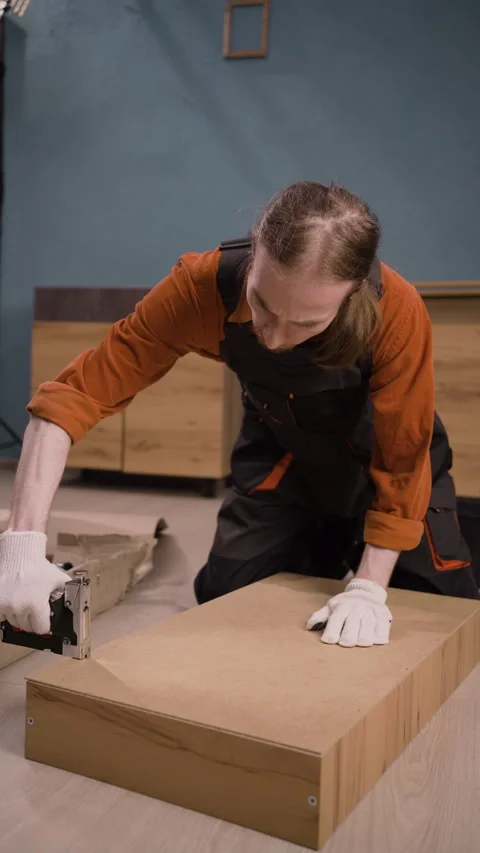 Furniture assembly process, male assembler using stapler to install cabinet part Stock Footage 310035361