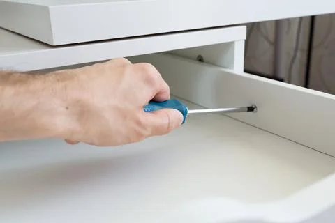 Furniture assembly process. Master assembles the bedside table. The worker uses Stock Photos
