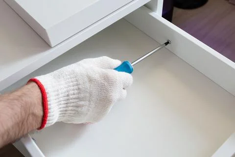 Furniture assembly process. Master in protective gloves assembles the bedside Foto stock