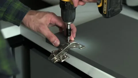 Furniture maker uses a screwdriver to attach hinge to a door of a cabinet Video stock 199282468