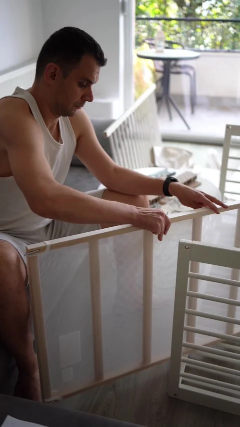 Future father assembling a white crib in a minimalist nursery room Stock Footage 329486404