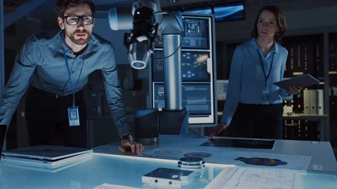 Futuristic Robotic Arm Moving and Placing a Metal Object. Senior Engineer Talks Stock Footage 105346895