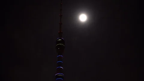 Futuristic TV tower is illuminated with multi color backlight near the full moon Stock Footage 106355503
