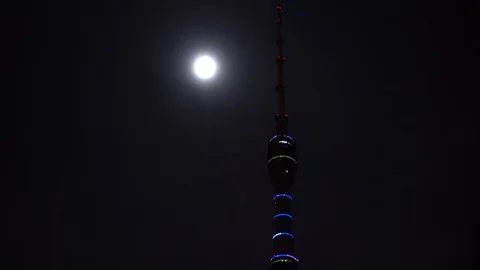 Futuristic TV tower is illuminated with multi color backlight near the full moon Video stock 106355854