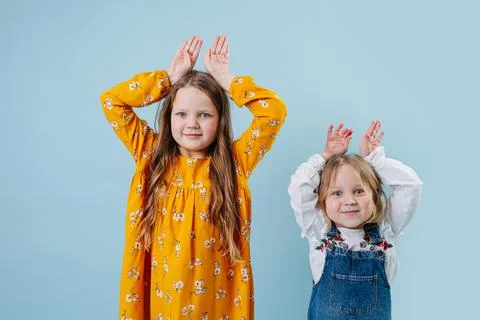 Fynny little sisters making easter bunny ears gesture with hands over blue Stock Photos