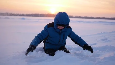 G child throwing snow over himself and enjoys it in winter park at sunset 库存影片 69856762