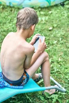 Gadget addiction. Wet boy sitting on sun lounger and playing on smartphone Stock Photos