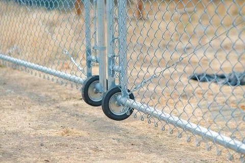 Galvanized rolling chain link gate wheels on dirt ground tracking Stock Photos