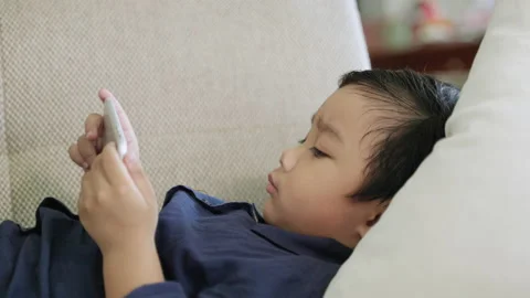 Game addict child is lying on the sofa playing games Stock Footage 151171270