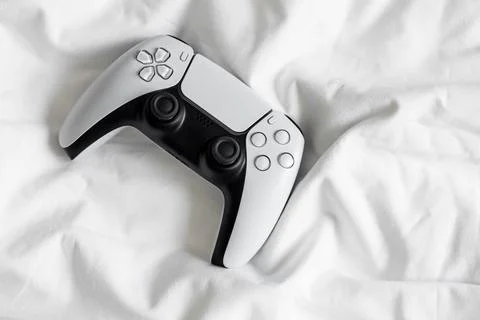 Game controller, lying on white sheets of bed at home. Stock Photos