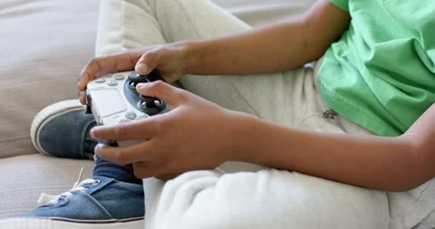 With game starting, child is manipulating white controller on sofa, thumbs Stock Footage 342928041