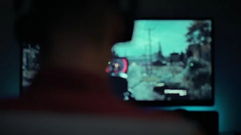 Gamer focused on action while playing shooting game on large screen at night Stock Footage 293735680