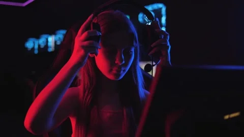 A gamer girl sits at a computer table and puts on headphones with a microphone. Stock Footage 332411195