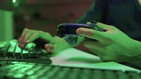 Gamer gripping red controller in dark hoodie, lowlit room with neon green PC and Stock Footage 347874778