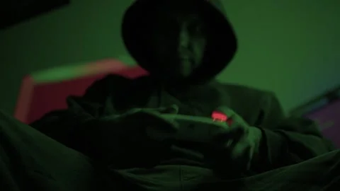 Gamer gripping red controller in dark hoodie, lowlit room with neon green PC and Stock Footage 347874815