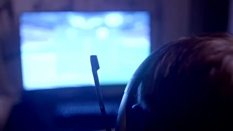 A gamer in a headset is engrossed in gameplay, surrounded by a dim light and the Stock Footage 295933014