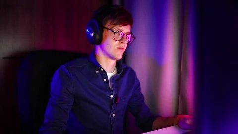 Gamer playing video games on a computer with headphones and using a colorful Stock Footage 143397671