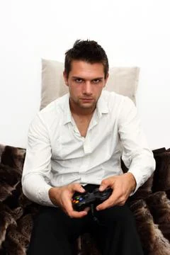 Gamer sitting on couch with controller and playing Stock Photos