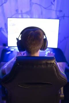 Gamer Using Headset in Front of Computer Screen with Blue Lighting Foto stock