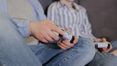 Gamers using console gamepads sitting on couch, playing video game at home Stock Footage 263980769