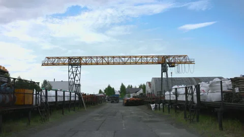 Gantry crane lowering hook over industrial storage yard with stacked pipes Stock Footage 346009888