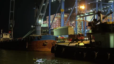 Gantry crane lowering a shipping container onto a cargo vessel at night. Vidéo 343140422