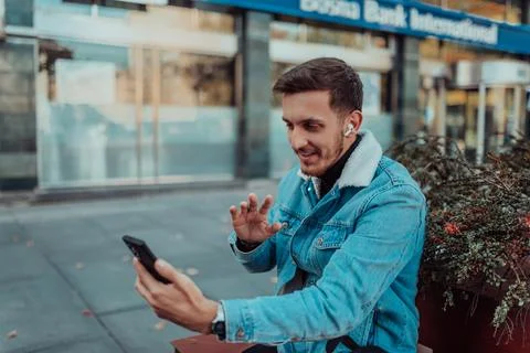 A gappy student sitting in a park using a smartphone and wireless headphones Foto stock