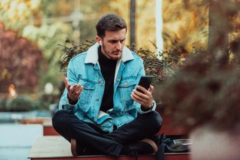 A gappy student sitting in a park using a smartphone and wireless headphones Stock Photos