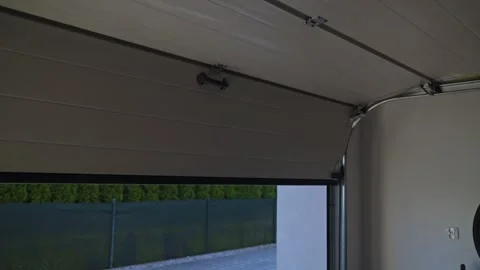 Garage door is closing from inside with yard, fence and trees visible outside Video stock 333484398