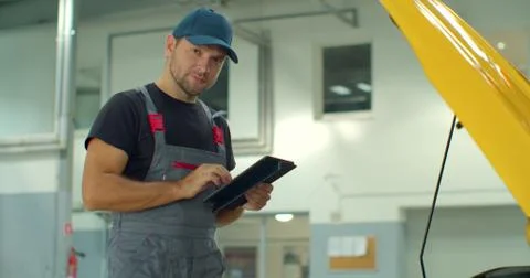 In a garage a mechanic using the tablet makes the oil and engine check to the Foto stock