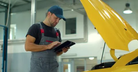 In a garage a mechanic using the tablet makes the oil and engine check to the Foto stock