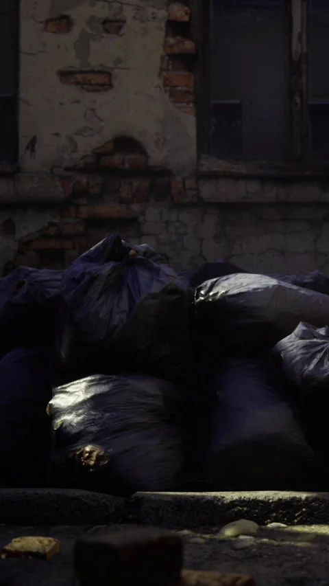 Garbage bags piled against an old building in a dimly lit area Stock Footage 334259697