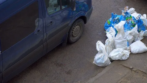 Garbage bags piled up on city sidewalks near a minibus Stock Footage 126592425