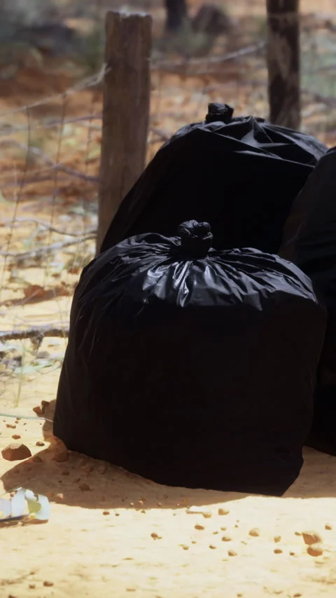 Garbage bags placed on ground near a fence in a dry outdoor area Stock Footage 334166644